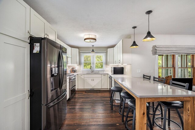 kitchen with a breakfast bar area, dark wood finished floors, a peninsula, a sink, and stainless steel appliances