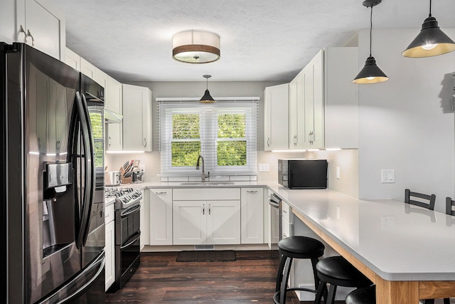 kitchen featuring a sink, a peninsula, range with two ovens, black refrigerator with ice dispenser, and dark wood-style flooring