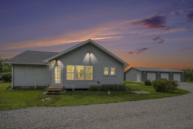 back of property at dusk with a garage, a lawn, an outdoor structure, and a shingled roof