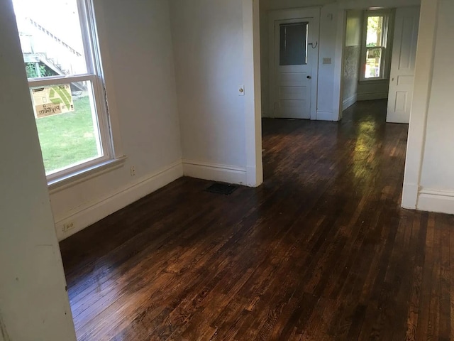 unfurnished room with dark wood finished floors, plenty of natural light, visible vents, and baseboards