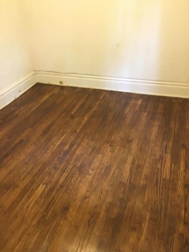 unfurnished room with dark wood-type flooring and baseboards