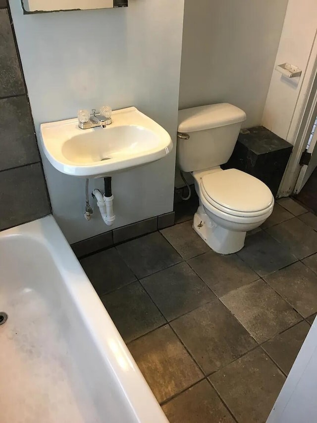 full bath featuring a bathtub, tile patterned floors, toilet, and a sink