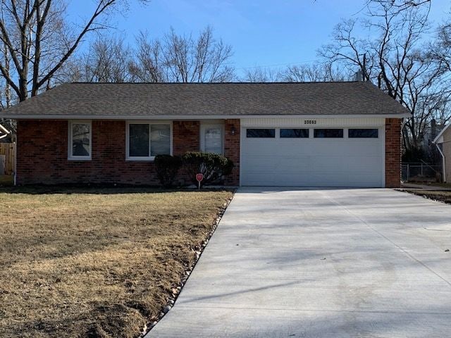 ranch-style house featuring brick siding, roof with shingles, concrete driveway, and an attached garage