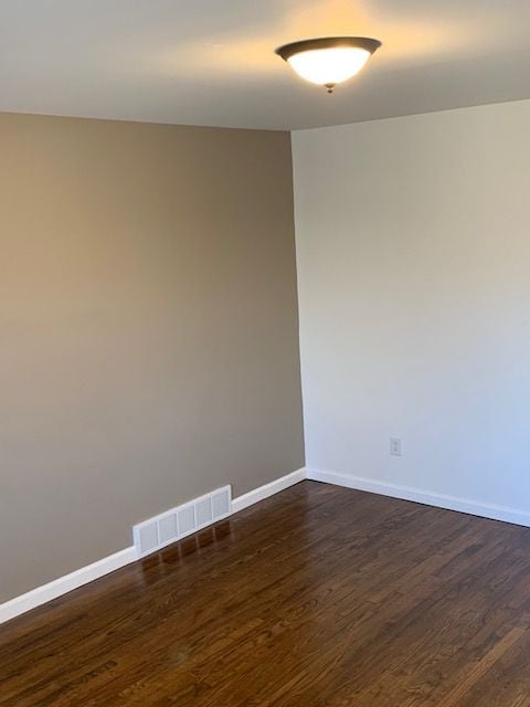 empty room featuring visible vents, baseboards, and dark wood-style flooring