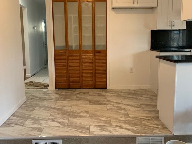 kitchen featuring dark countertops, visible vents, glass insert cabinets, baseboards, and white cabinetry