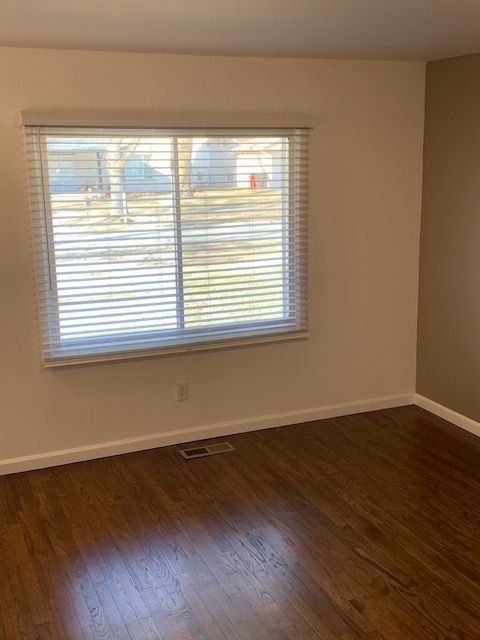 unfurnished room featuring dark wood-style floors, a healthy amount of sunlight, visible vents, and baseboards