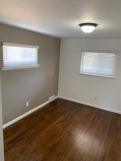 empty room featuring dark wood-type flooring, visible vents, baseboards, and a wealth of natural light