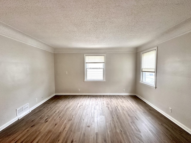 spare room with dark wood-style floors, visible vents, baseboards, and a wealth of natural light