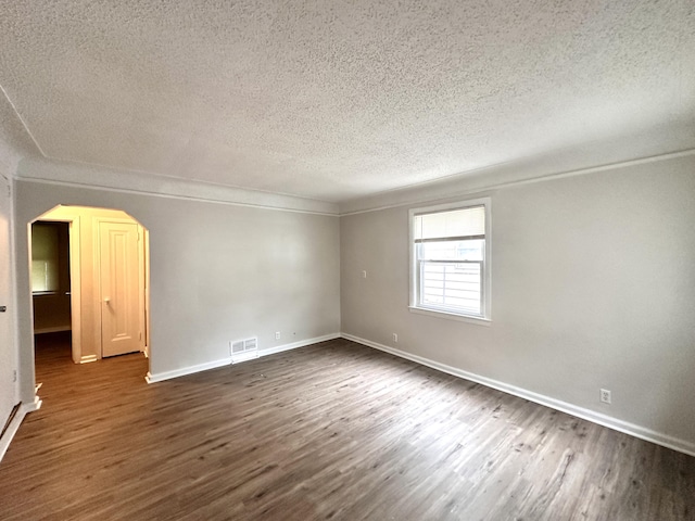 unfurnished room with dark wood-type flooring, visible vents, arched walkways, and baseboards