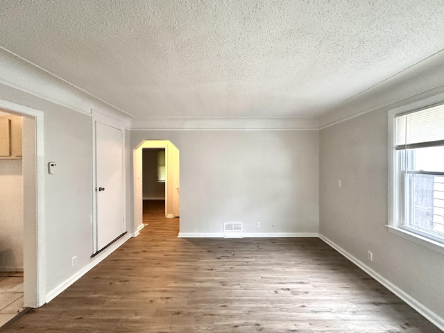 spare room with arched walkways, a textured ceiling, baseboards, and wood finished floors