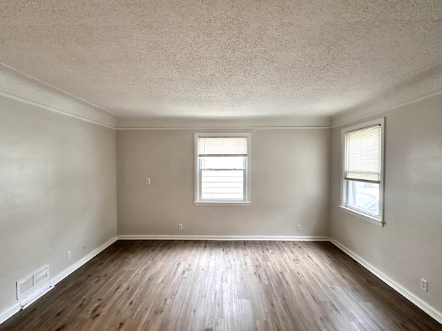 unfurnished room with plenty of natural light, dark wood-style floors, visible vents, and baseboards