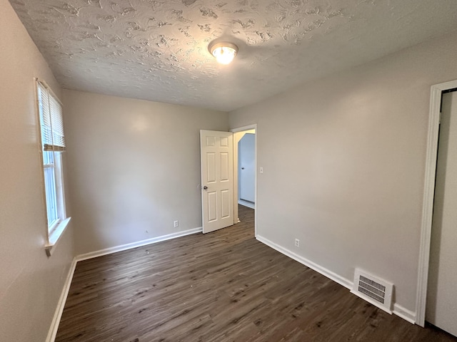 unfurnished room featuring visible vents, a textured ceiling, baseboards, and dark wood-style flooring