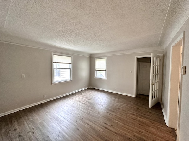 empty room featuring ornamental molding, dark wood-style floors, baseboards, and a textured ceiling