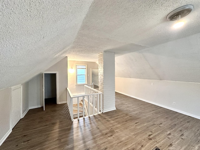 additional living space featuring vaulted ceiling, a textured ceiling, baseboards, and wood finished floors