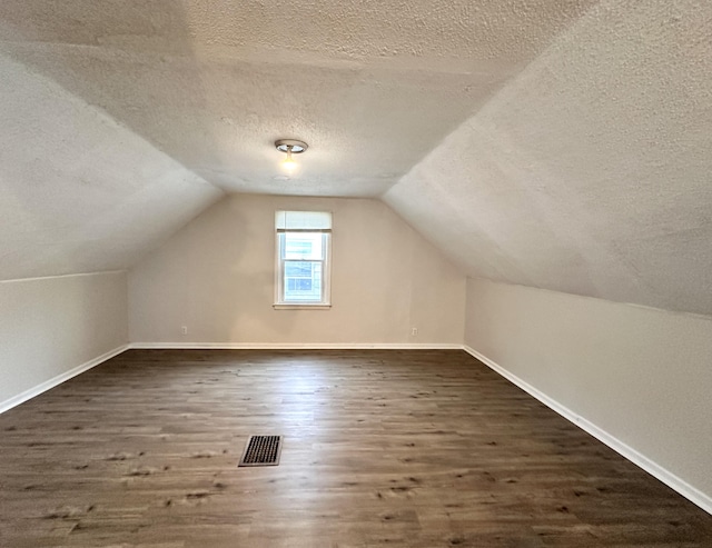 additional living space featuring visible vents, a textured ceiling, wood finished floors, baseboards, and lofted ceiling