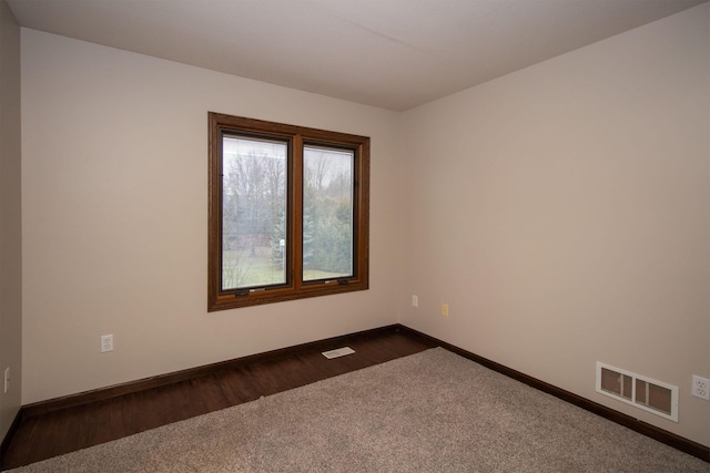 empty room featuring visible vents, baseboards, and dark wood-type flooring