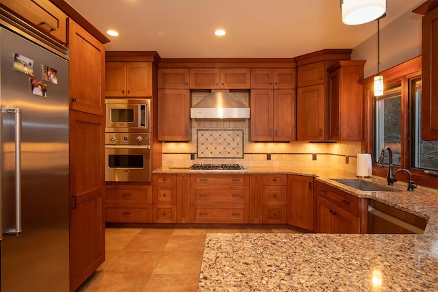 kitchen featuring built in appliances, brown cabinets, wall chimney exhaust hood, and a sink