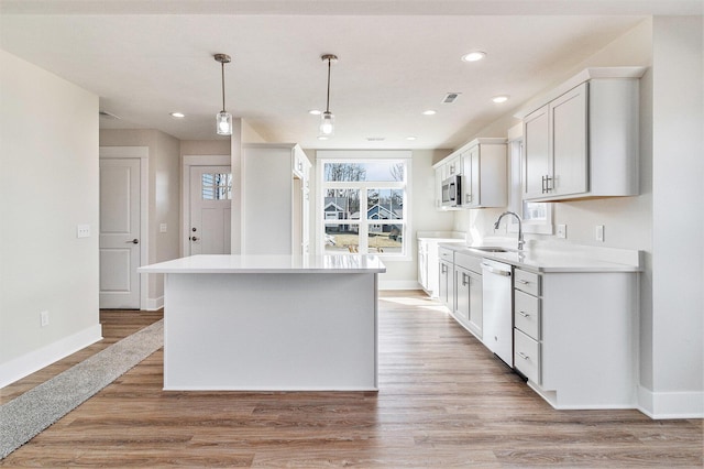 kitchen with a sink, stainless steel microwave, a center island, light wood finished floors, and dishwasher