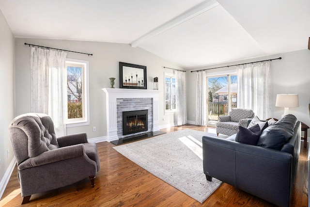 living room featuring a glass covered fireplace, baseboards, wood finished floors, and vaulted ceiling with beams