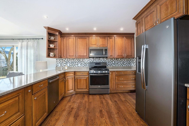 kitchen featuring dark wood finished floors, brown cabinets, appliances with stainless steel finishes, and light stone counters