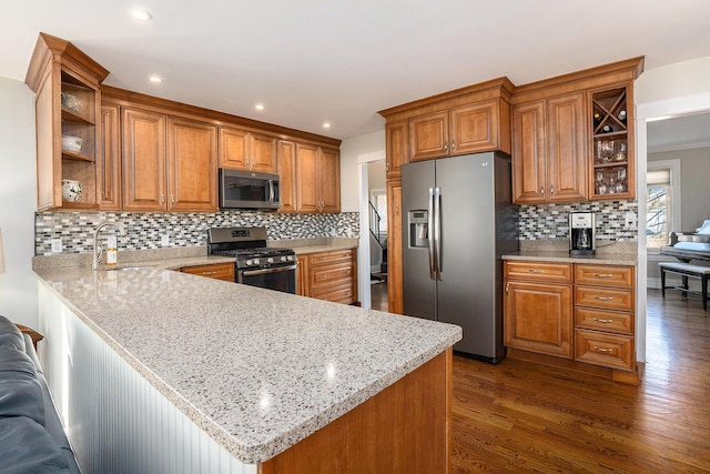 kitchen with brown cabinetry, a peninsula, a sink, dark wood-type flooring, and appliances with stainless steel finishes