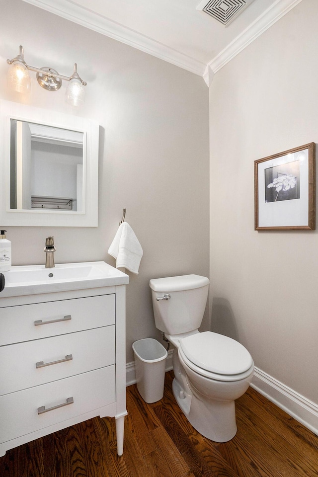 half bathroom with wood finished floors, baseboards, visible vents, ornamental molding, and toilet