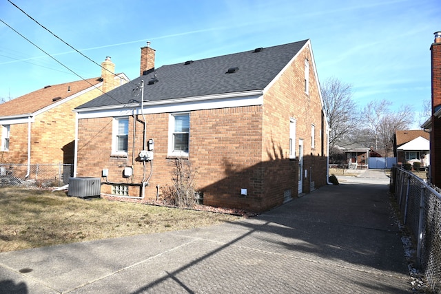 back of property with brick siding, a chimney, a shingled roof, and fence