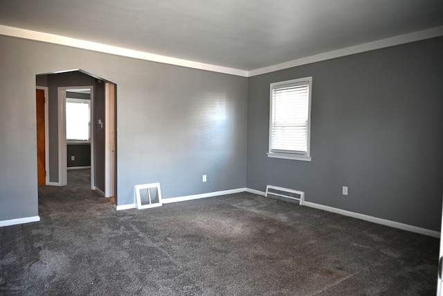 empty room featuring arched walkways, visible vents, dark carpet, and baseboards