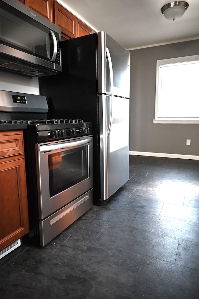 kitchen with baseboards, brown cabinets, dark countertops, and appliances with stainless steel finishes