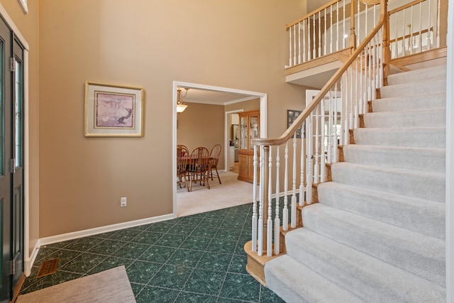 entryway with crown molding, stairs, a high ceiling, and baseboards