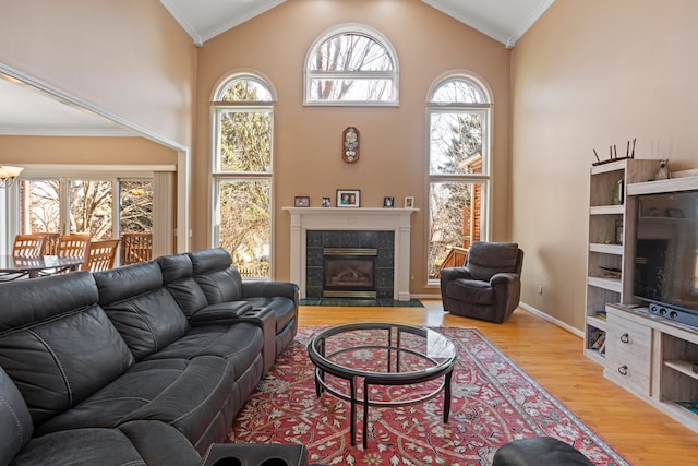 living area with crown molding, high vaulted ceiling, wood finished floors, and a tile fireplace