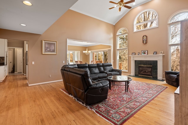 living area with a wealth of natural light, a tiled fireplace, high vaulted ceiling, and light wood-type flooring