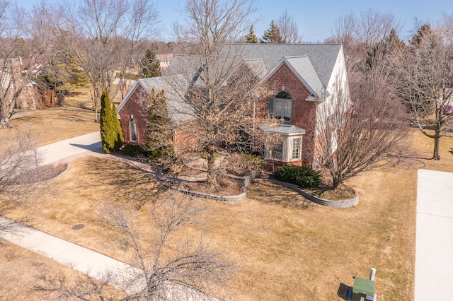 view of front of home with brick siding, roof with shingles, and a front yard