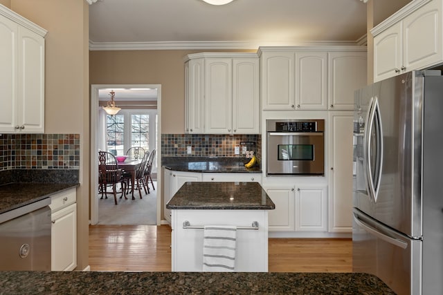 kitchen featuring light wood-style flooring, tasteful backsplash, stainless steel appliances, dark stone counters, and crown molding