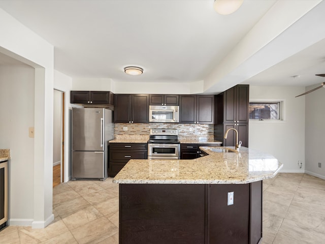 kitchen featuring a sink, appliances with stainless steel finishes, decorative backsplash, light stone countertops, and dark brown cabinets