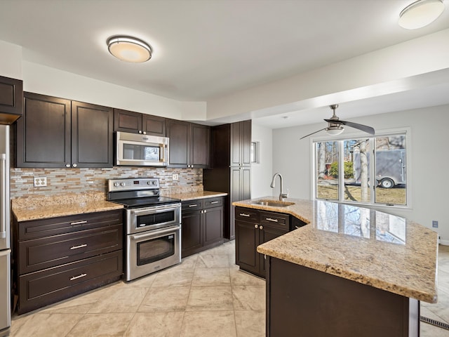 kitchen featuring a sink, backsplash, stainless steel appliances, dark brown cabinetry, and light stone countertops