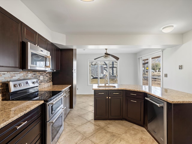 kitchen with light stone countertops, a sink, dark brown cabinetry, appliances with stainless steel finishes, and tasteful backsplash