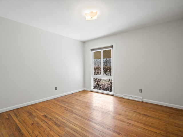 empty room with a baseboard radiator, baseboards, and wood finished floors