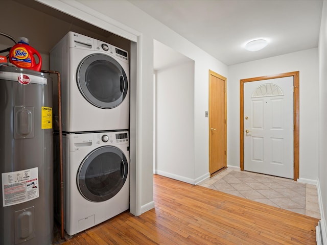 washroom with baseboards, light wood finished floors, laundry area, electric water heater, and stacked washer / dryer