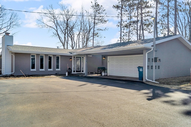 single story home with aphalt driveway, roof with shingles, an attached garage, brick siding, and a chimney