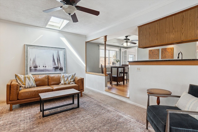 living room featuring baseboards, ornamental molding, carpet floors, a skylight, and a textured ceiling