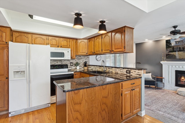 kitchen with a brick fireplace, a peninsula, brown cabinetry, white appliances, and a sink