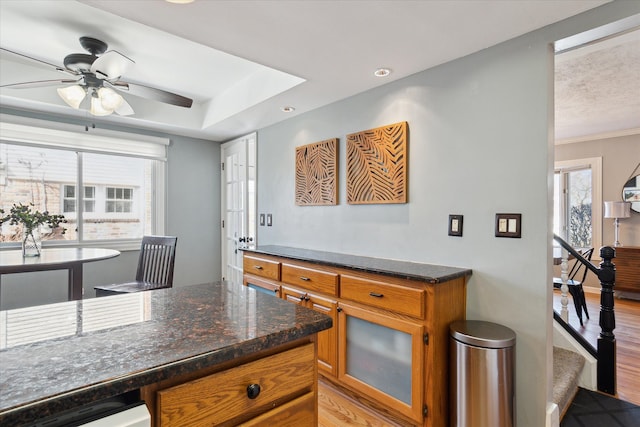 kitchen featuring light wood finished floors, ceiling fan, glass insert cabinets, a raised ceiling, and brown cabinets