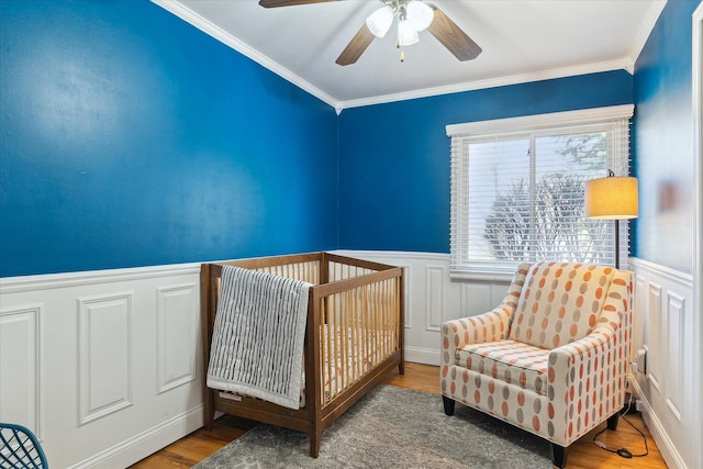 bedroom with a ceiling fan, wood finished floors, wainscoting, and ornamental molding