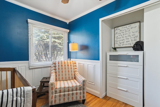 living area featuring a wainscoted wall, wood finished floors, ornamental molding, and a ceiling fan