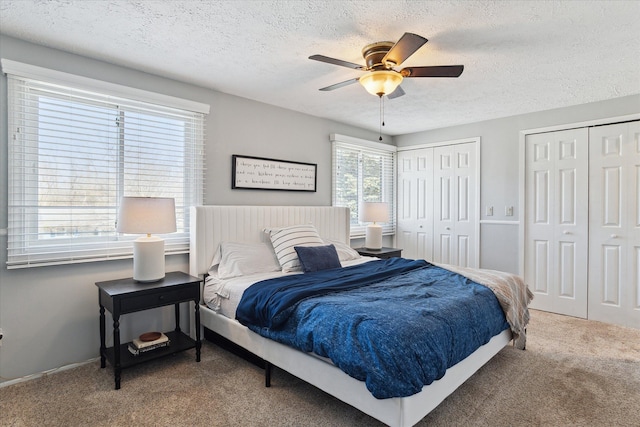 carpeted bedroom with a ceiling fan, multiple closets, and a textured ceiling