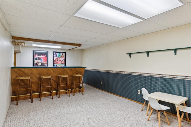 interior space with carpet flooring, a bar, a paneled ceiling, and a wainscoted wall