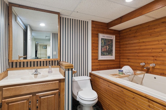 bathroom featuring a drop ceiling, toilet, a bath, and vanity