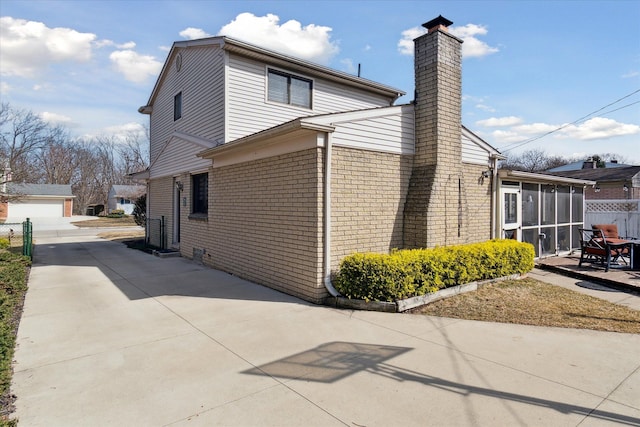 view of side of home with an outdoor structure, a sunroom, brick siding, a chimney, and a patio area