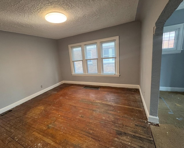 spare room with hardwood / wood-style floors, visible vents, baseboards, and a textured ceiling